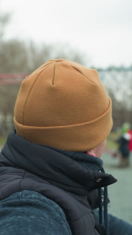close-up of a coach performing pull-ups, pausing after the fifth rep to rest, while looking left and then front, the background shows a blurred view of other people at the outdoor gym