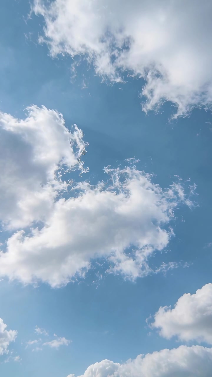 Video verticale: Gruppo di nuvole alla deriva che cambiano forma nel cielo blu, muovendosi con la brezza a sbuffi