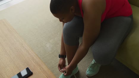 mujer afroamericana de talla grande practicando yoga, atando cordones en la sala de estar