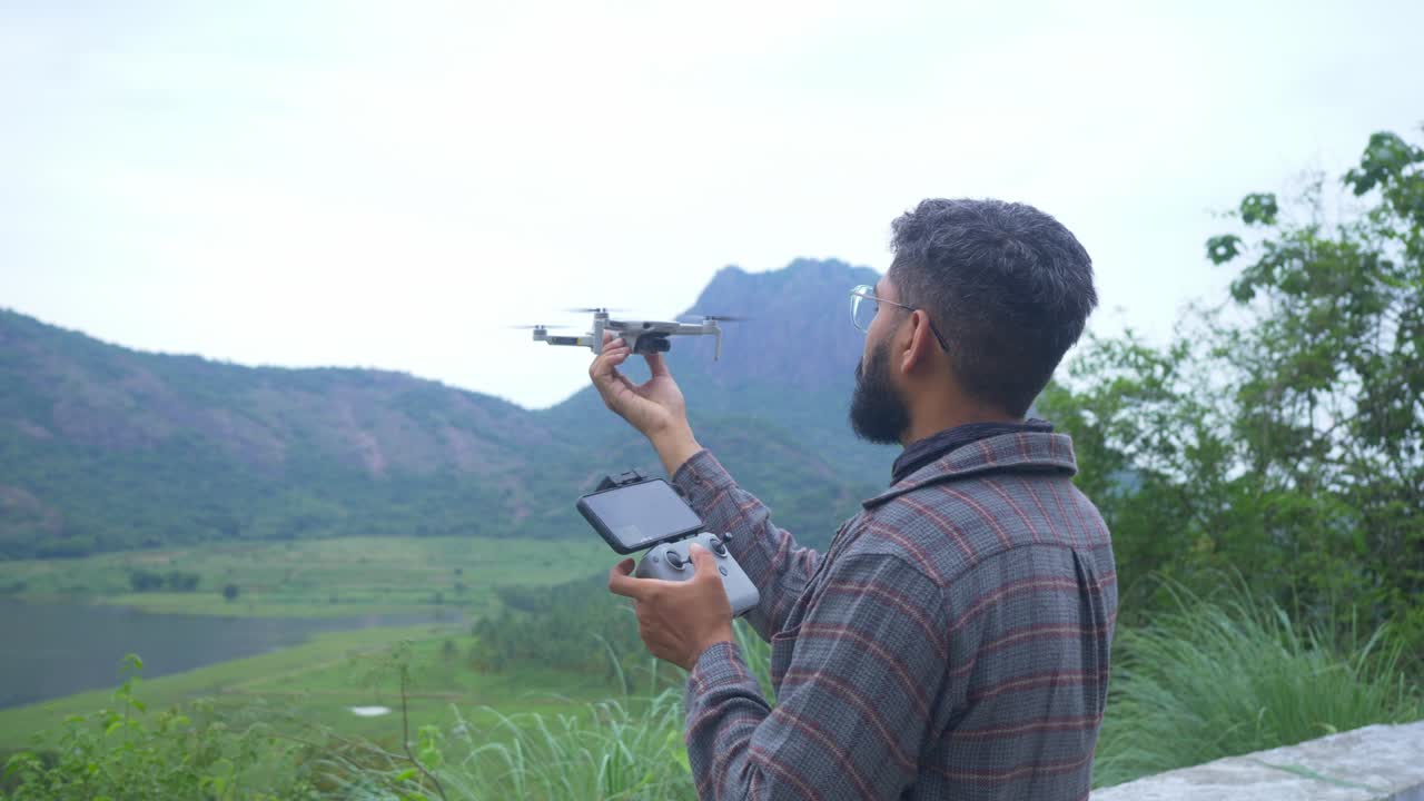 un joven indio aterrizando su mini dron en un paisaje forestal salvaje de los ghats occidentales, india