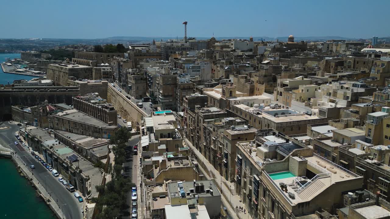 Aerial view of Valletta, Malta under a clear blue sky. Historic cityscape with limestone buildings, fortifications, and Mediterranean coastline captured from above
