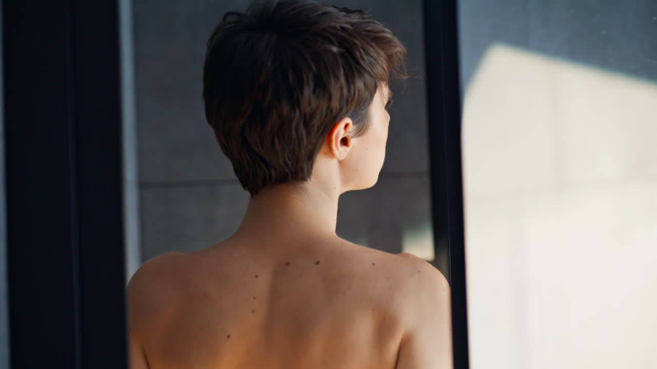 Nærbilde av korthåret brunette som tar av seg badekåpen. Kvinne med bare skuldre under en spa-økt.