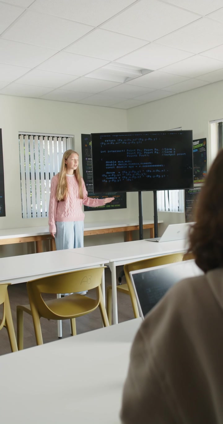Video verticale: Presentatrice adolescente che inizia a parlare in classe, spiegando codice sullo schermo, con spazio copia.
