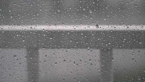 Raindrops-Dripping-On-The-Surface-of-Glass-Window-on-blury-background,-Steel-Railings-Outside-of-top-floor-appartment-balcony-in-Seoul,-South-Korea