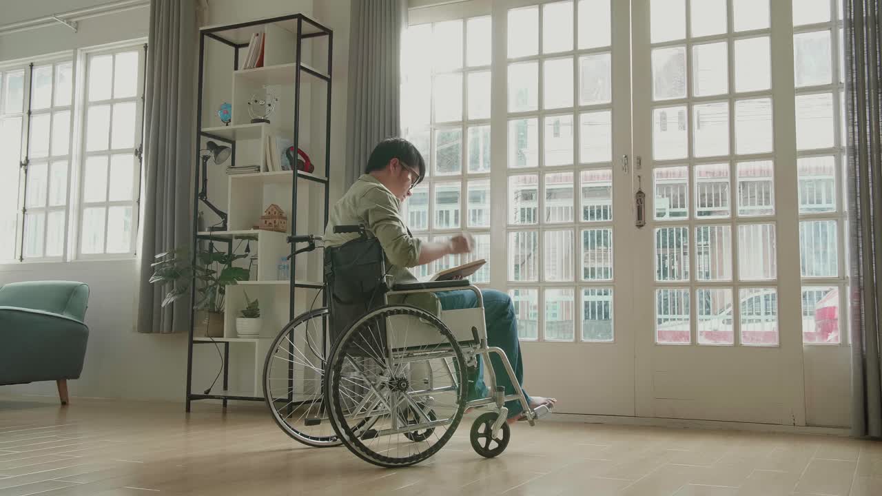 Asian Man Sitting In A Wheelchair Reading Book Near Door In The House