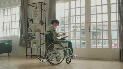 asian man sitting in a wheelchair reading book near door in the house