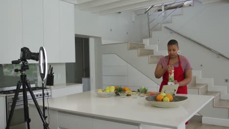 feliz mujer afroamericana de talla grande con delantal, haciendo un vlog de cocina con cámara en la cocina