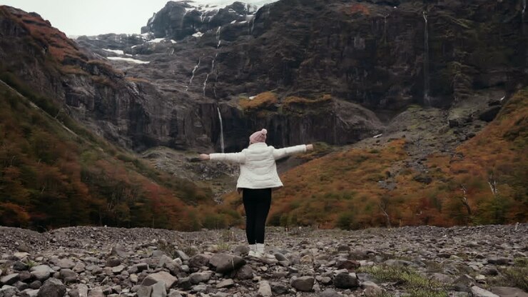 Travel woman raises her hands in beautiful landscape with waterfall and mountains