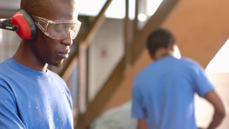 working african american male coworkers shaping planks in workshop, with goggles and wood boards