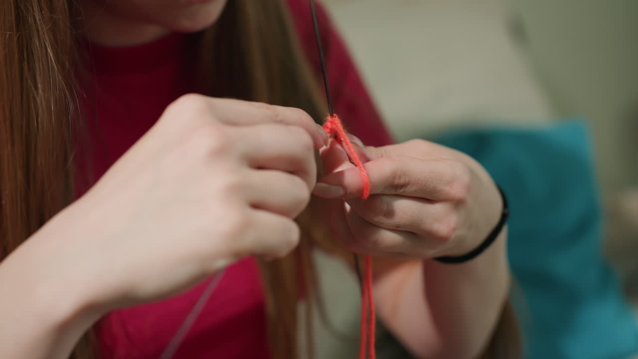 Mujer tejiendo cómodamente, dedos femeninos entrelazando hilo brillante, movimientos detallados de las manos creando lana colorida y vibrante, vista cercana de una mujer creando hábilmente con lana brillante