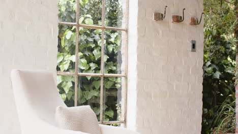 cozy white chair by window with lush green garden view outside, at home