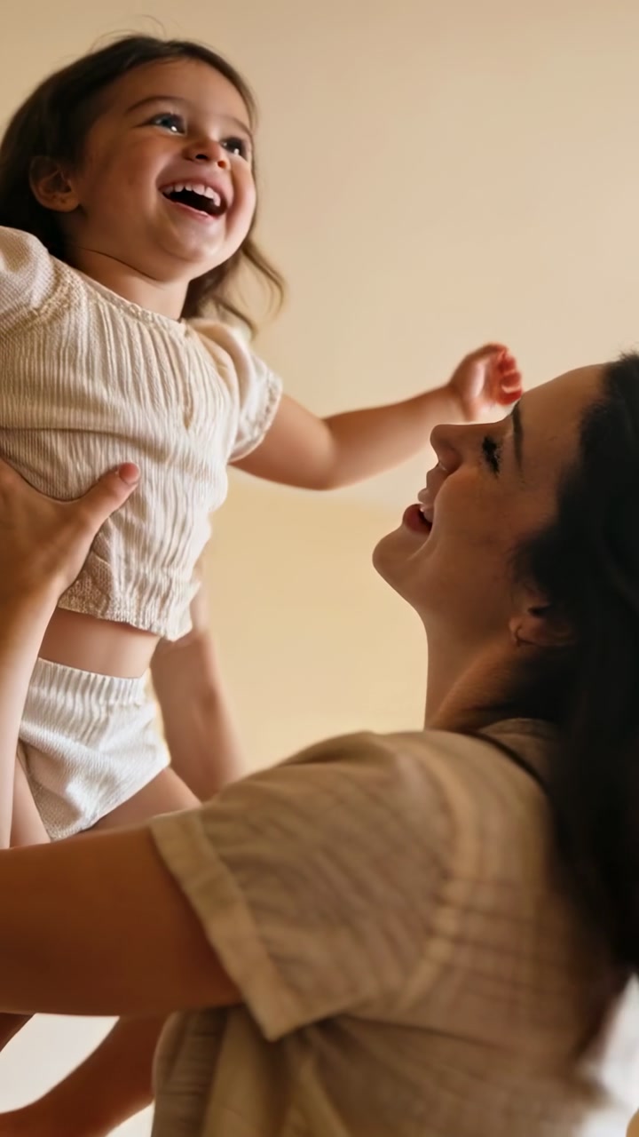 Vertical video: Mother lifting toddler up at home, hands holding hips as toddler laughing