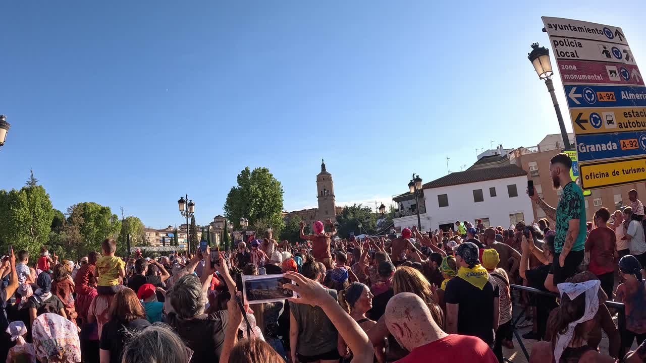 Guadix Festival of Cascamorras 2024. Crowd of people covered in colors dancing and jumping in frotr of the cathedral.