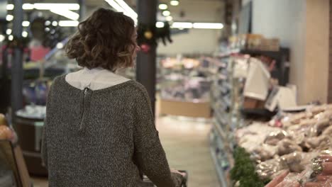Rare-view-of-a-woman-is-driving-shopping-trolley-through-food-department-in-supermarket-and-looking-around,-picking-bag-with-potatos.-Pretty-girls,-everyday-life-and-buying-products-concept