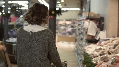 rare view of a woman is driving shopping trolley through food department in supermarket and looking around, picking bag with potatos. pretty girls, everyday life and buying products concept