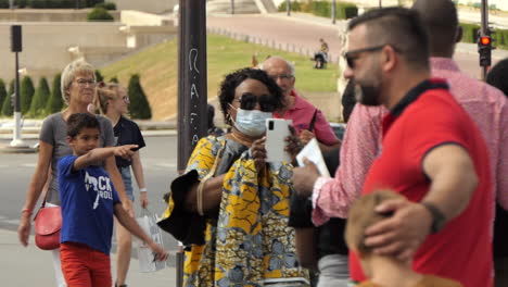 African tourist with a protective mask on her face taking a picture of the Eiffel Tower from the Iena Bridge in Paris, summer 2020.