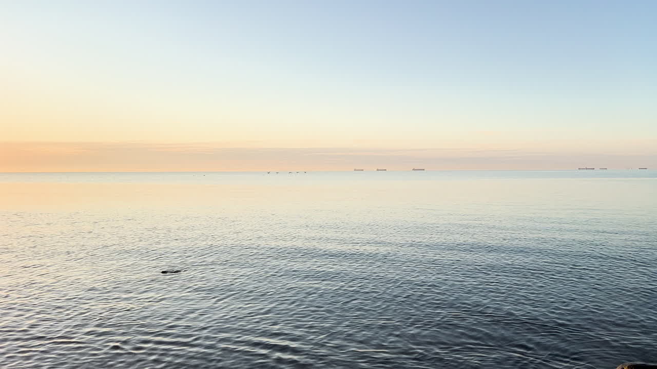 The sea mirrors the soft hues of dusk, offering a tranquil vista with distant ships on the horizon