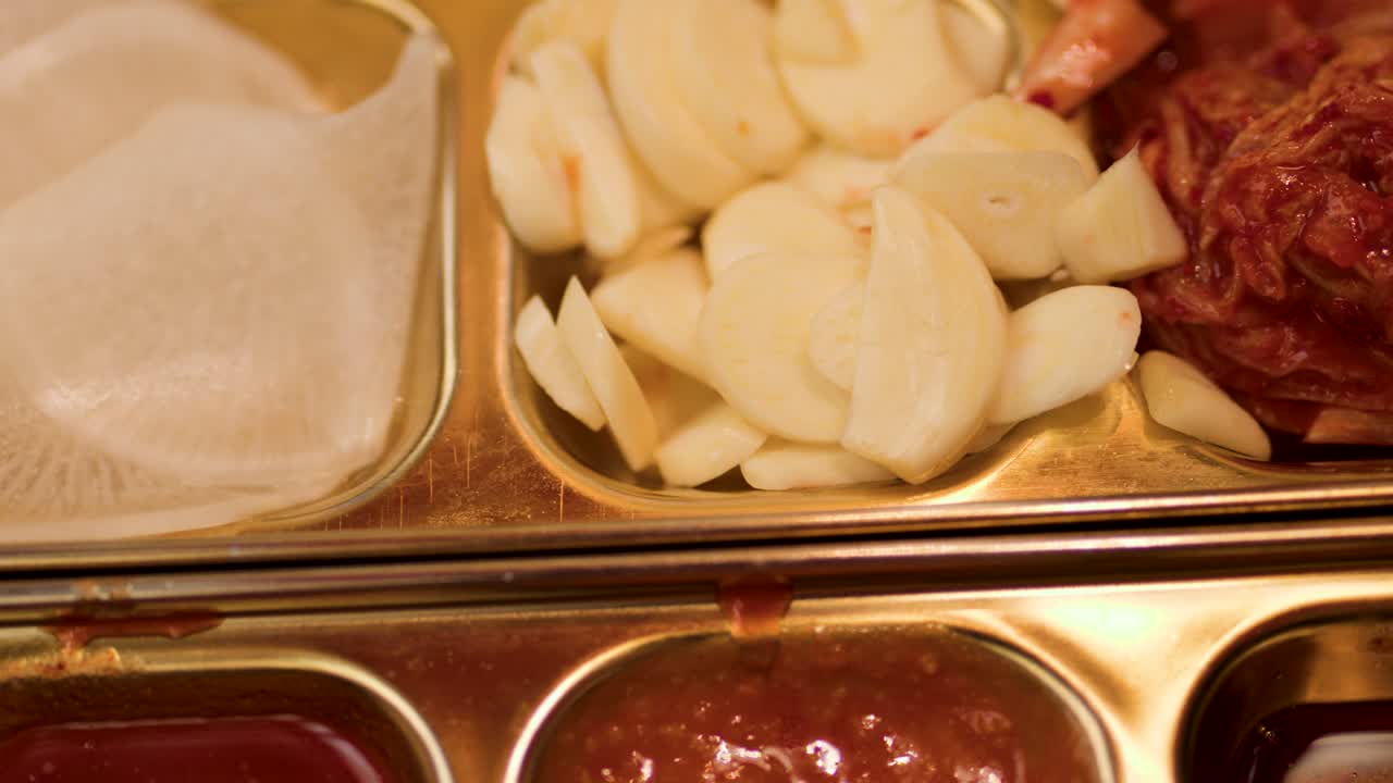 Camera pans across garlic, kimchi, pickled radish, dipping sauces in warm restaurant lighting