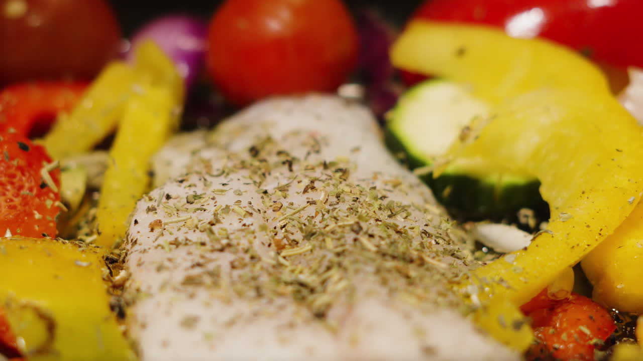 Erbe aromatiche che cadono al rallentatore su filetti di merluzzo atlantico pescato in natura con verdure della dieta mediterranea. Peperoni, cipolle, zucchine, pomodori. Videografia di cibo sano di alta qualità.