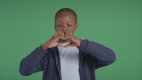 Studio-Portrait-Of-Boy-Making-Heart-Shape-With-Hands-Against-Green-Background-1