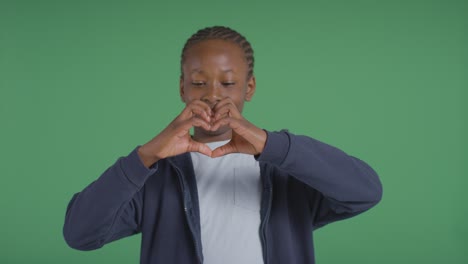 studioporträt eines jungen, der mit den händen vor grünem hintergrund eine herzform macht 1