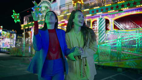 happy friends enjoying evening at amusement park. cheerful girls laughing walk