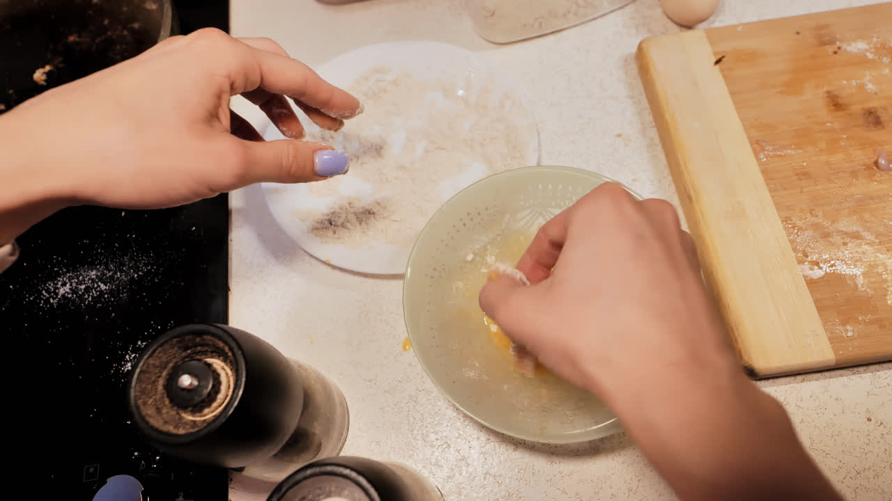 Messy countertop as young woman coats raw chicken for rustic homemade frying