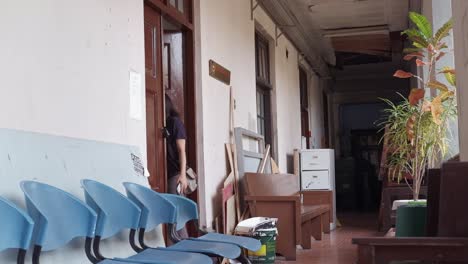 Static-wide-shot-of-asian-woman-exit-room-into-cluttered-hallway-and-stands