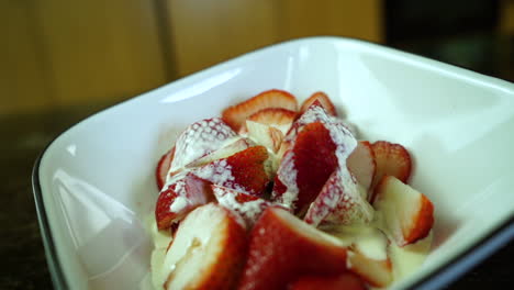 la crema espesa gotea lentamente sobre las fresas maduras cortadas en un bol