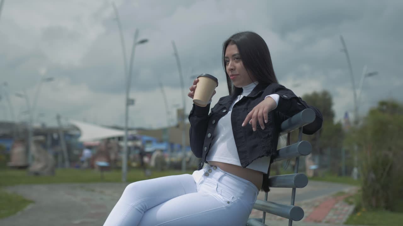 Ung latinamerikansk kvinde slapper af på en parkbænk