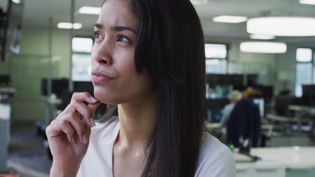 mujer pensativa frotándose la barbilla en la oficina