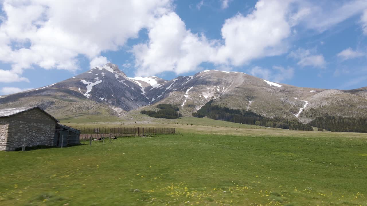이탈리아 아브루초의 시골 시골에 있는 그란 사소 산맥으로 둘러싸인 초원 계곡에 있는 오래된 셰퍼드 쉼터의 광각 장면