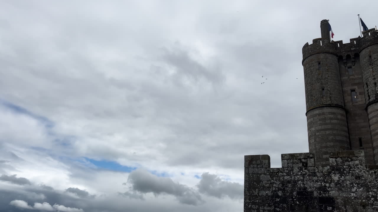 View of a medieval castle with cloudy sky and French flags at Mont Saint-Michel