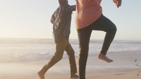 Smiling-senior-african-american-couple-holding-hands-and-running-on-sunny-beach