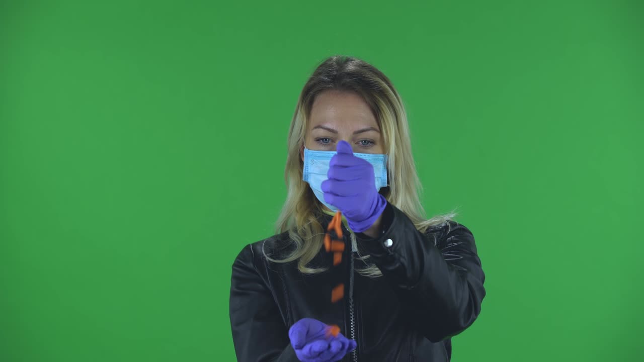 retrato de una hermosa joven con una máscara de protección facial médica vertiendo medicina de mano en mano para evitar la propagación del coronavirus. rubia con cabello suelto en una chaqueta negra y vaqueros en una pantalla verde en el estudio. protección de la salud corona