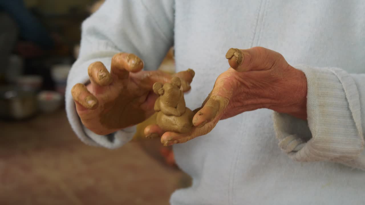 Primo piano delle mani di una donna che modella flauti di argilla a forma di animale a Thanh Ha, un popolare souvenir turistico in Vietnam.