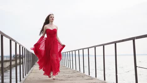 woman in a red dress walking on a pier