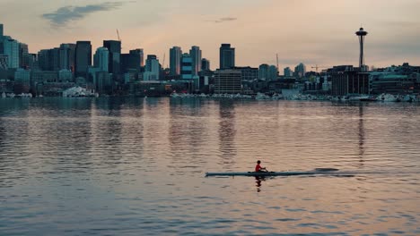 a single rower in a boat paddles their way across lake union in seattle with the skyline and space needle in the background