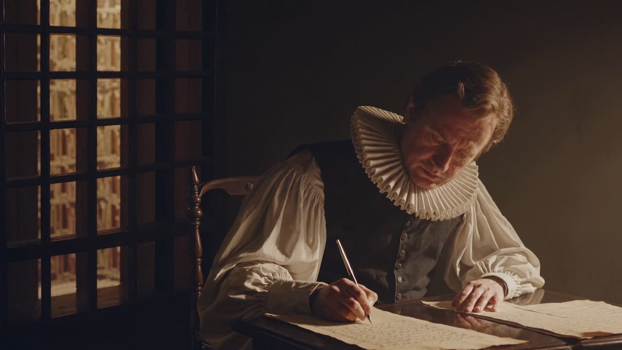 A dimly lit video scene captures a man in period attire writing at a desk, shot from a side angle