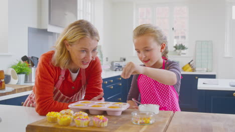 Grandmother-With-Granddaughter-Decorating-Homemade-Cakes-On-Kitchen-Counter-At-Home