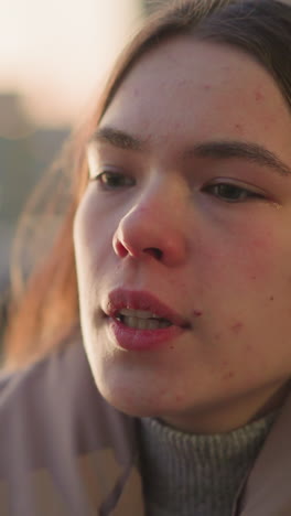 un primer plano de una mujer joven con una chaqueta de melocotón, con una expresión contemplativa en su rostro, perdida en profundos pensamientos. el fondo urbano borroso mejora el enfoque en su estado de ánimo introspectivo