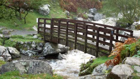 Idílico-Puente-De-Madera-Sobre-La-Cascada-Del-Valle-Que-Cae-En-Cascada-En-Un-Poderoso-Río-Que-Fluye,-Carro-Lento-A-La-Derecha