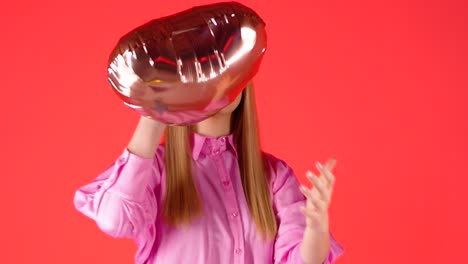 mujer rubia lanzando dos globos dorados en forma de corazón, estado de ánimo de san valentín, fotografía de estudio con fondo de color rojo