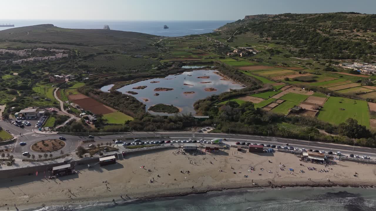 Vista aerea con drone della baia di Ghadira e della riserva naturale a Mellieha, Malta, che mette in risalto la spiaggia sabbiosa, il piccolo lago, i campi circostanti e la pittoresca costa mediterranea in un vivace paesaggio invernale