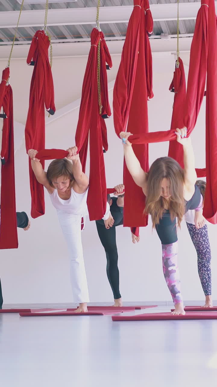 ladies group practice aerial yoga warrior asana standing on one leg and holding long red hammock in new gym