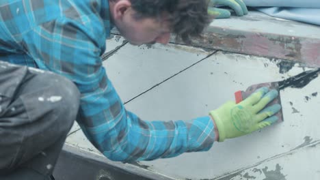 a young man smoothes mastic sealant into boat plank seams