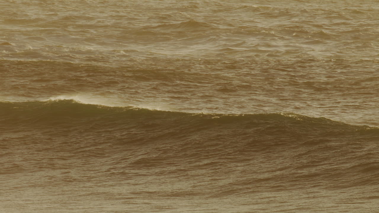 Surfer disappears behind thick curtain of golden backlit wave as it builds and mist rises
