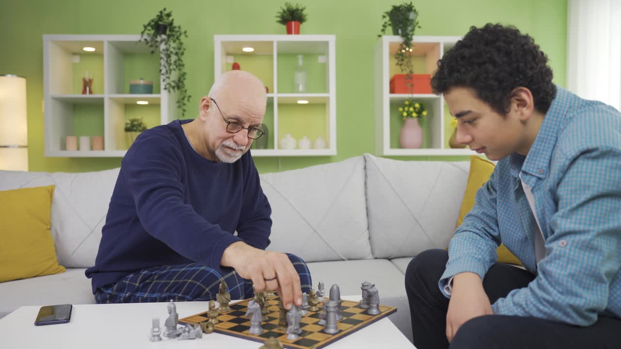 joven jugando al ajedrez con su abuelo moderno en la sala de estar.