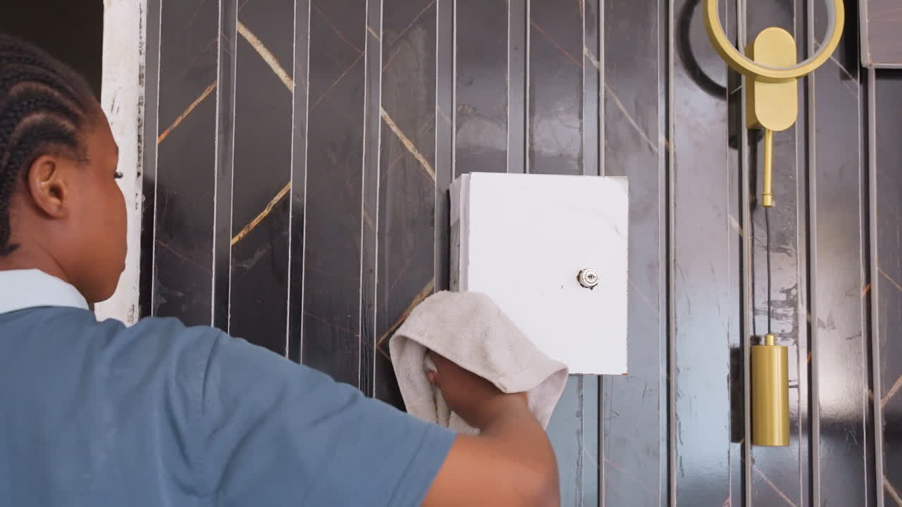 Cleaning young girl. Girl tidying house door. Child wiping door with cloth peacefully. Young girl cleaning door in daylight with care. Girl in uniform cleans house entrance with cloth during daytime