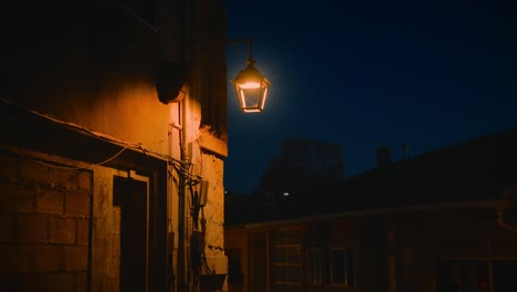 Old-Outdoor-Lamp-Lighting-Up-Back-of-Building,-Sinister-Feel-Handheld-Shot